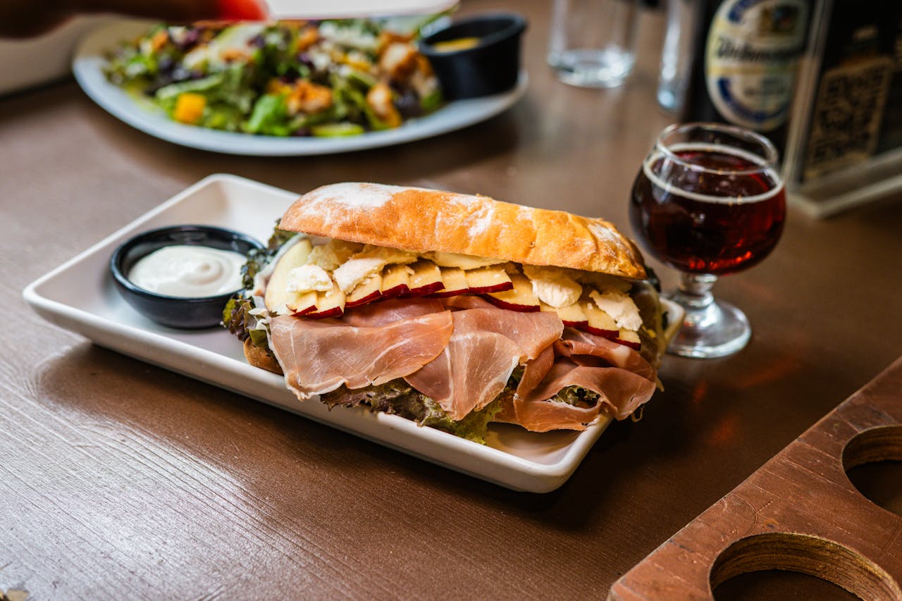 Delicious ciabatta sandwich with prosciutto, cheese, and apples paired with craft beer.